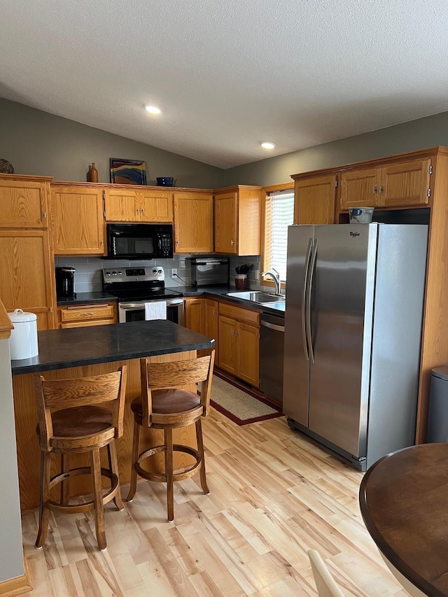 728 7th St, Litchfield, MN 55355 - kitchen featuring appliances with stainless steel finishes, a sink, dark countertops, light wood-style flooring, and vaulted ceiling