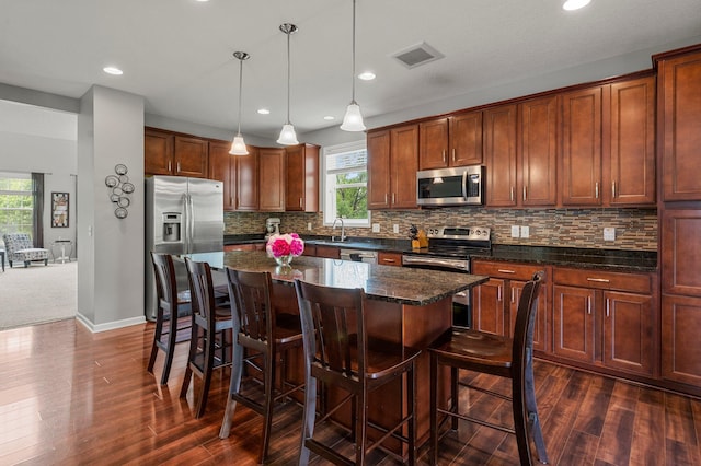 8607 Portage Ln E, Shakopee, MN 55379 - kitchen with stainless steel appliances, a kitchen island, dark wood-type flooring, a kitchen breakfast bar, and tasteful backsplash