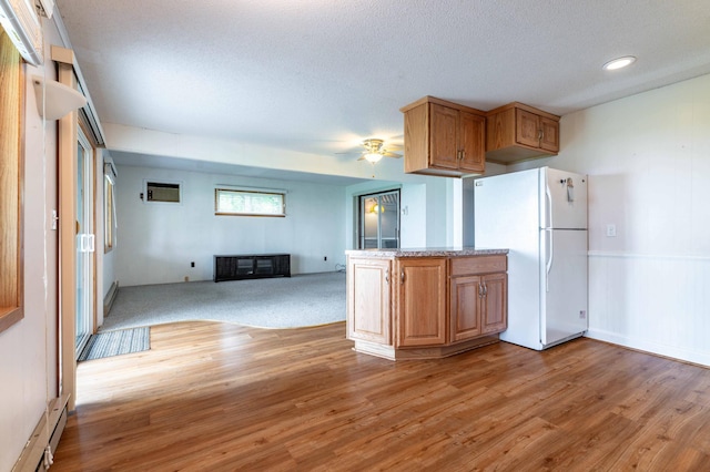 27326 Cloverleaf Ln, Everts Twp, MN 56515 - kitchen featuring freestanding refrigerator, a glass covered fireplace, a ceiling fan, brown cabinetry, and light wood finished floors