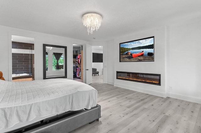 7447 213th St N, Forest Lake, MN 55025 - bedroom with light wood-type flooring, a glass covered fireplace, a spacious closet, a chandelier, and baseboards