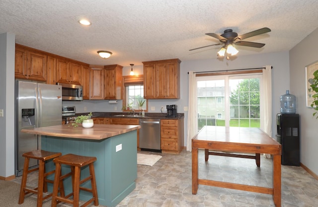1046 Roosevelt St S, Cambridge, MN 55008 - kitchen featuring appliances with stainless steel finishes, a textured ceiling, ceiling fan, brown cabinetry, and a breakfast bar