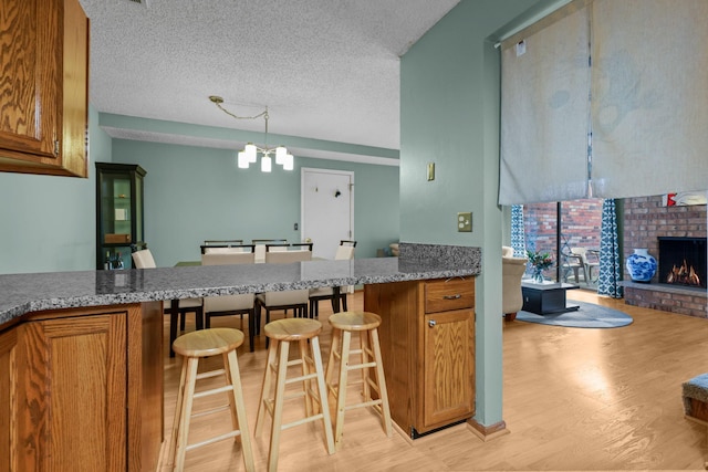 3625 Gettysburg Ave S Unit 40, Saint Louis Park, MN 55426 - kitchen featuring brown cabinets, light wood-style flooring, a breakfast bar area, a chandelier, and a fireplace