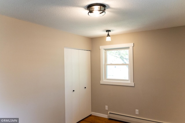 1322 17th St W, Hastings, MN 55033 - unfurnished bedroom featuring a closet, dark wood-style floors, a baseboard radiator, a textured ceiling, and baseboards