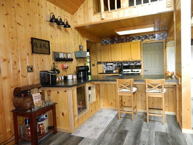 3749 Grizzly Ln, Barnum Twp, MN 55707 - kitchen with wooden ceiling, wood finished floors, dark countertops, wood walls, and a kitchen bar