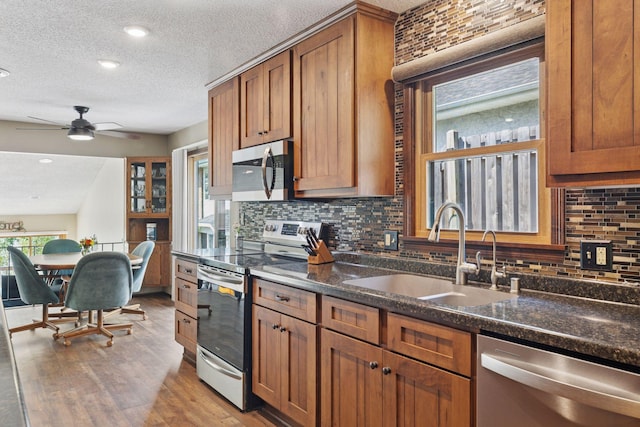 7469 Fernbrook Ln N, Maple Grove, MN 55311 - kitchen featuring appliances with stainless steel finishes, a sink, a textured ceiling, brown cabinetry, and decorative backsplash