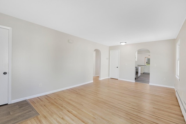 111 4th St, Kenyon, MN 55946 - spare room with arched walkways, a baseboard radiator, light wood-style flooring, and baseboards