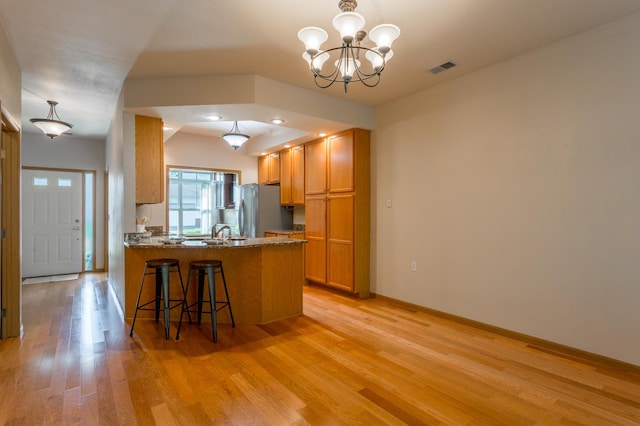 2230 Lower Afton Rd E, Saint Paul, MN 55119 - kitchen featuring freestanding refrigerator, light wood-type flooring, a peninsula, brown cabinetry, and a kitchen bar