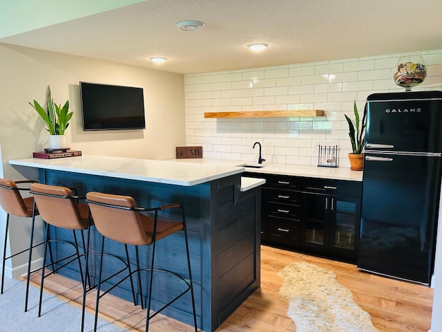 8633 Ambergate Dr, Victoria, MN 55386 - kitchen featuring freestanding refrigerator, dark cabinets, a kitchen bar, light wood-type flooring, and a peninsula