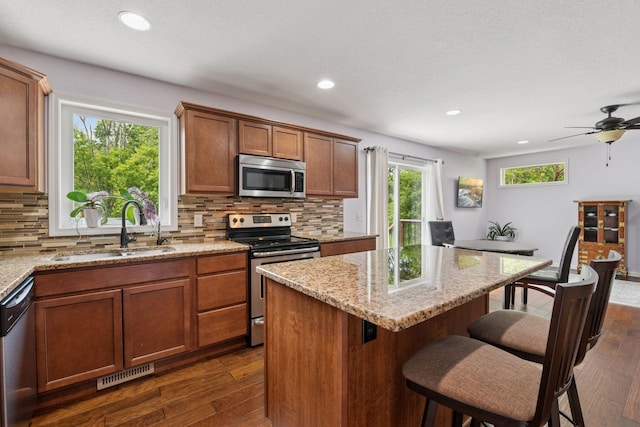 5110 Woodridge Rd, Minnetonka, MN 55345 - kitchen with appliances with stainless steel finishes, a sink, dark wood-type flooring, backsplash, and a kitchen breakfast bar