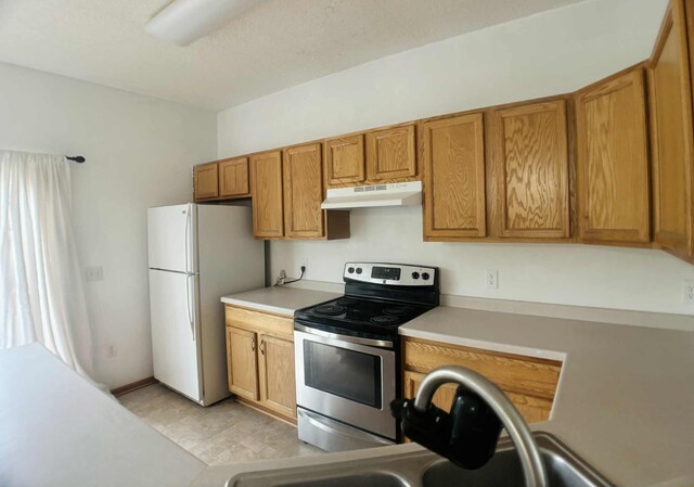1366 Phalen Blvd, Saint Paul, MN 55106 - kitchen with stainless steel range with electric cooktop, under cabinet range hood, freestanding refrigerator, light countertops, and brown cabinets