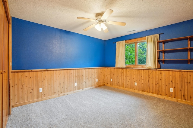 881 217th St, Osceola, WI 54020 - empty room with wainscoting, a textured ceiling, a ceiling fan, wood walls, and carpet floors