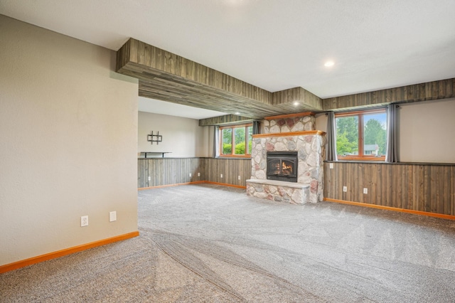 881 217th St, Osceola, WI 54020 - unfurnished living room featuring carpet floors, wood walls, a stone fireplace, baseboards, and a wainscoted wall