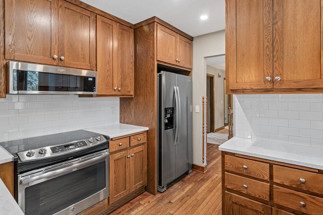 6230 Elm Ridge Cir, Corcoran, MN 55340 - kitchen with stainless steel appliances, brown cabinetry, light wood-type flooring, backsplash, and light countertops