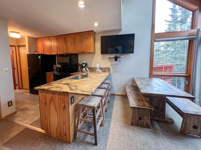 529 Moose Mountain Dr, Lutsen Twp, MN 55615 - kitchen with black appliances, a sink, brown cabinets, light stone countertops, and a kitchen bar
