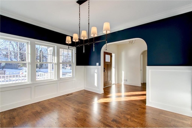 TBB403 College St, Northfield, MN 55057 - unfurnished dining area featuring arched walkways, crown molding, wainscoting, a chandelier, and a decorative wall