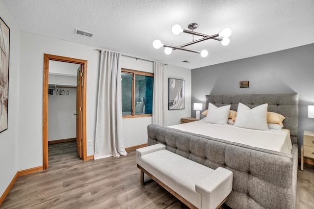 11260 Hidden Oaks Ct N, Champlin, MN 55316 - bedroom with wood finished floors, a spacious closet, a chandelier, a textured ceiling, and baseboards