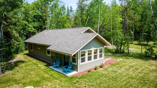 15989 Lost Oaks Dr SE, Cass Lake, MN 56633 - back of property with a shingled roof, a patio area, a lawn, and a forest view