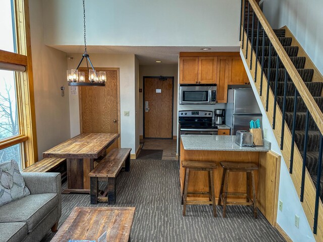 122 Bridge Run Ln Unit A, Lutsen Twp, MN 55615 - kitchen with stainless steel appliances, brown cabinets, a towering ceiling, a chandelier, and a peninsula