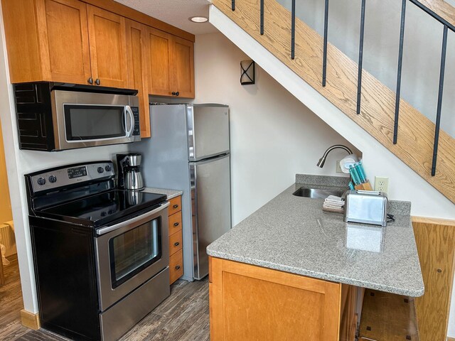 122 Bridge Run Ln Unit A, Lutsen Twp, MN 55615 - kitchen with stainless steel appliances, a sink, brown cabinetry, dark wood-style floors, and light stone countertops