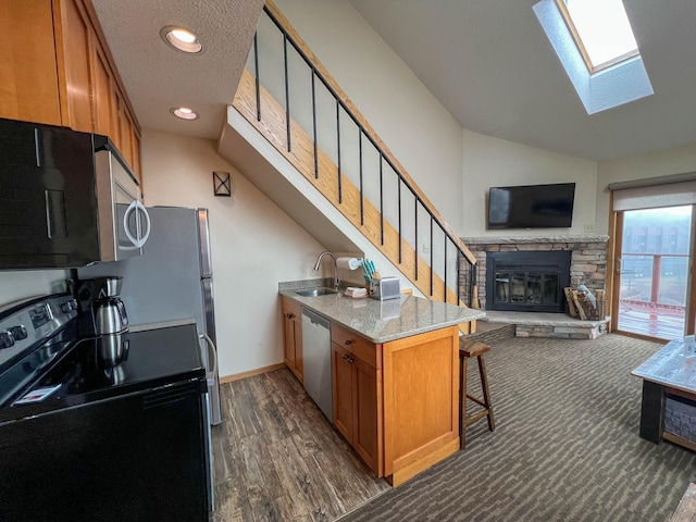 122 Bridge Run Ln Unit A, Lutsen Twp, MN 55615 - kitchen with stainless steel appliances, a skylight, brown cabinetry, open floor plan, and a stone fireplace