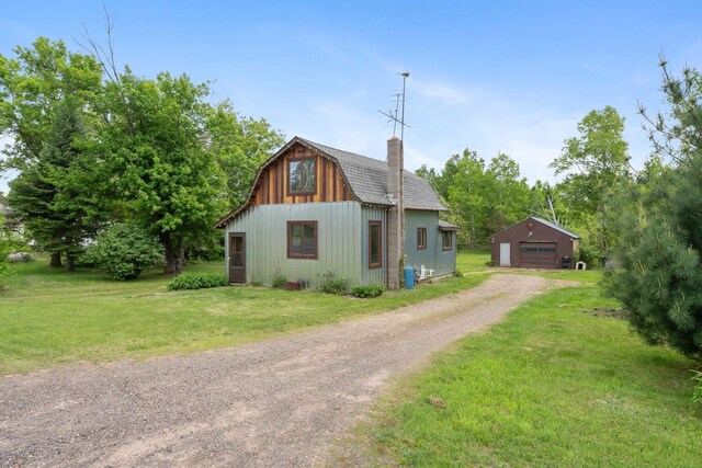 7627 Main St, Danbury, WI 54830 - view of front facade featuring a garage, an outdoor structure, dirt driveway, a front yard, and a gambrel roof