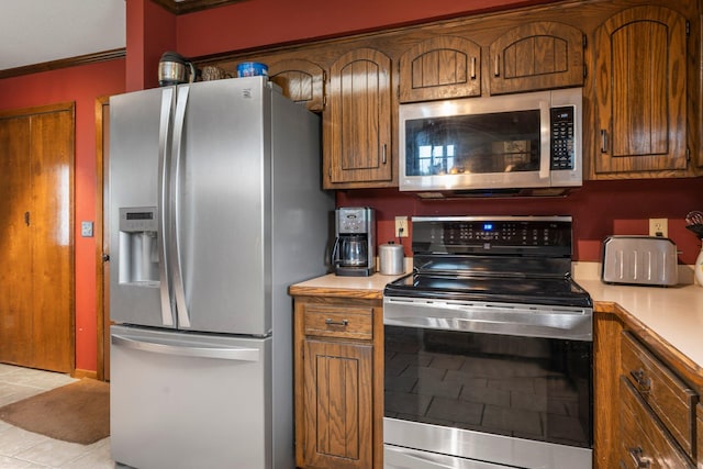 7567 Lent Trl, Lent Twp, MN 55079 - kitchen featuring appliances with stainless steel finishes, light countertops, brown cabinetry, crown molding, and light tile patterned floors
