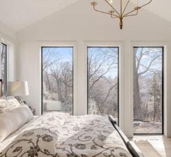 bedroom with vaulted ceiling, access to outside, multiple windows, and a chandelier