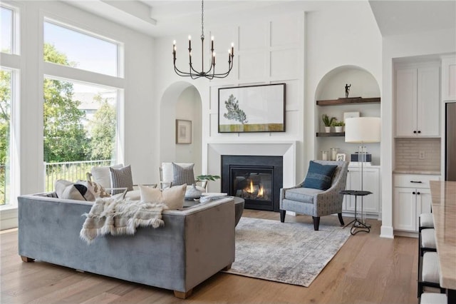 living room featuring a towering ceiling, a chandelier, a glass covered fireplace, light wood-style flooring, and arched walkways