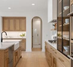 kitchen with arched walkways, gas stovetop, a sink, baseboards, and light wood-style floors