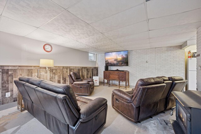 3886 Eagle Rd, Willmar, MN 56201 - living area featuring concrete floors, a paneled ceiling, a wainscoted wall, a wood stove, and wooden walls