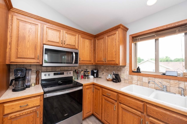 1406 English Ave NW, New Prague, MN 56071 - kitchen featuring stainless steel appliances, lofted ceiling, tasteful backsplash, light countertops, and brown cabinets