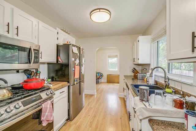 3807 Hubbard Ave N, Robbinsdale, MN 55422 - kitchen featuring stainless steel appliances, arched walkways, light wood-style floors, and white cabinetry