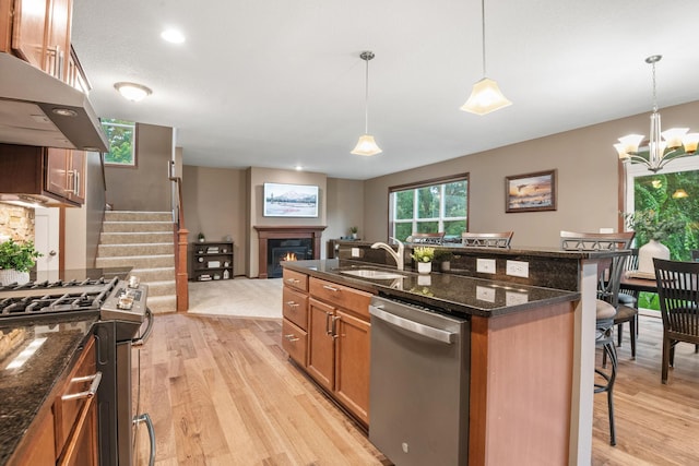 4027 148th Ln NE, Ham Lake, MN 55304 - kitchen with stainless steel appliances, exhaust hood, a kitchen breakfast bar, a lit fireplace, and light wood finished floors