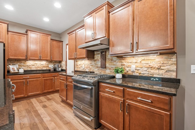 4027 148th Ln NE, Ham Lake, MN 55304 - kitchen featuring gas stove, under cabinet range hood, light wood finished floors, tasteful backsplash, and dark stone counters