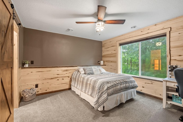 4027 148th Ln NE, Ham Lake, MN 55304 - bedroom with wood walls, carpet, a textured ceiling, a barn door, and ceiling fan