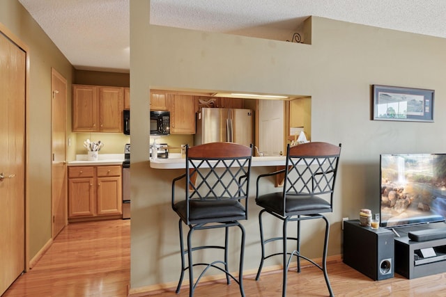 14617 Evergreen Trl Unit 75, Apple Valley, MN 55124 - kitchen with black microwave, freestanding refrigerator, a breakfast bar, a textured ceiling, and light wood finished floors