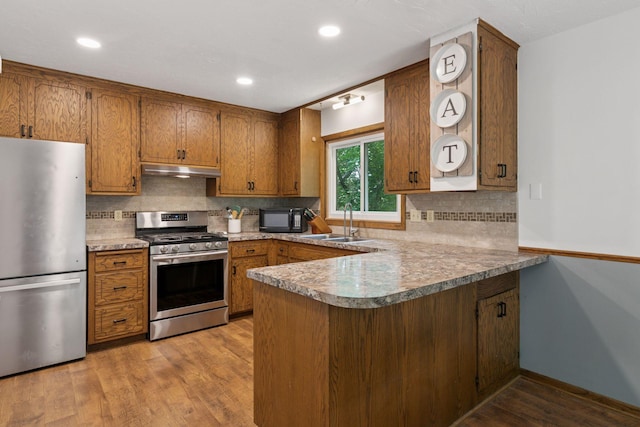 3228 Spruce Trl SW, Prior Lake, MN 55372 - kitchen featuring appliances with stainless steel finishes, under cabinet range hood, a peninsula, brown cabinets, and decorative backsplash