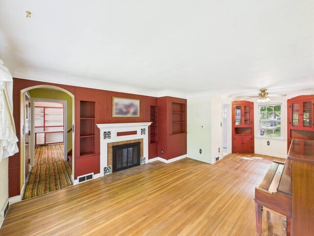 1538 8th Ave SE, Saint Cloud, MN 56304 - unfurnished living room featuring arched walkways, light wood finished floors, built in shelves, a ceiling fan, and a fireplace