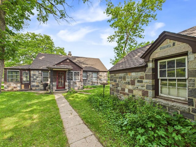 1538 8th Ave SE, Saint Cloud, MN 56304 - english style home featuring stone siding, a front lawn, a shingled roof, and a chimney