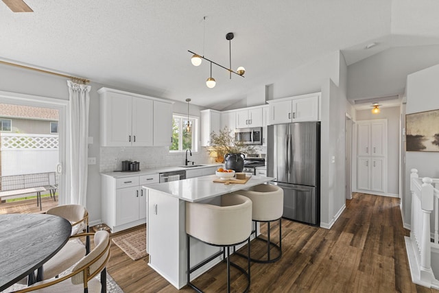 104 Bison Ct, Buffalo, MN 55313 - kitchen featuring appliances with stainless steel finishes, backsplash, vaulted ceiling, white cabinetry, and decorative light fixtures