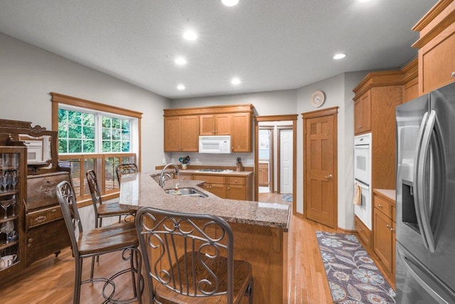 10426 Hidden Oaks Ln N, Champlin, MN 55316 - kitchen featuring white appliances, brown cabinets, light wood-style flooring, recessed lighting, and a kitchen island with sink