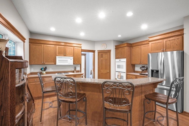 10426 Hidden Oaks Ln N, Champlin, MN 55316 - kitchen with white appliances, wood finished floors, a center island, recessed lighting, and a breakfast bar area
