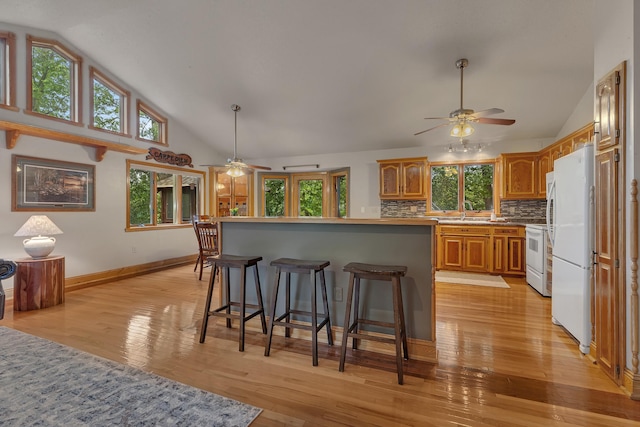 14789 Fireside Cir, Cold Spring, MN 56320 - kitchen with a ceiling fan, a breakfast bar area, tasteful backsplash, brown cabinetry, and high vaulted ceiling