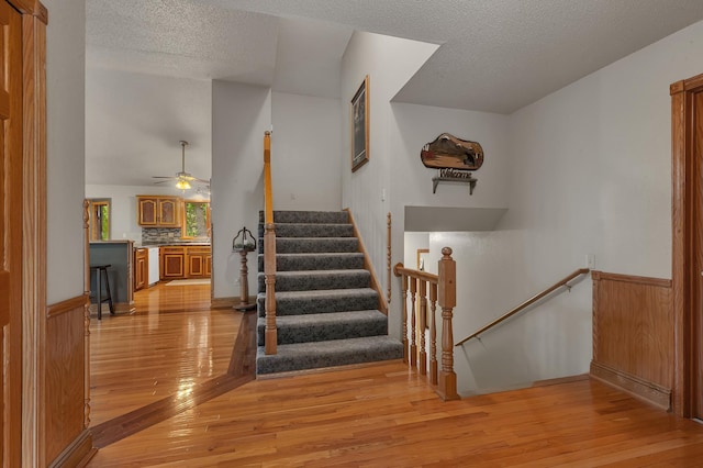 14789 Fireside Cir, Cold Spring, MN 56320 - staircase featuring wood finished floors, a textured ceiling, a wainscoted wall, and a ceiling fan