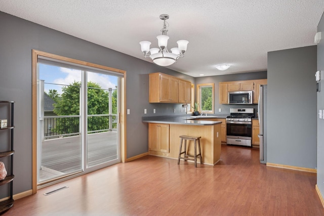 19470 Zumbro Ct NW, Elk River, MN 55330 - kitchen with appliances with stainless steel finishes, a peninsula, light brown cabinets, a chandelier, and wood finished floors