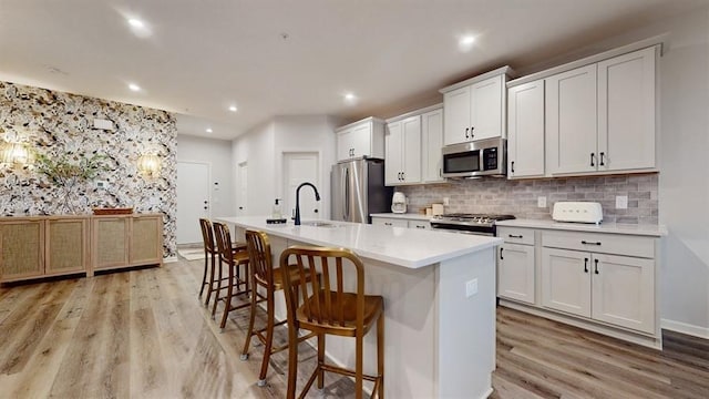 6775 Bluestem Way, Minnetrista, MN 55331 - kitchen featuring stainless steel appliances, a sink, light wood-style flooring, an island with sink, and a kitchen breakfast bar