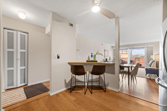26 10th St W Unit 706, Saint Paul, MN 55102 - kitchen with light wood finished floors, a textured ceiling, ceiling fan, a kitchen breakfast bar, and baseboards