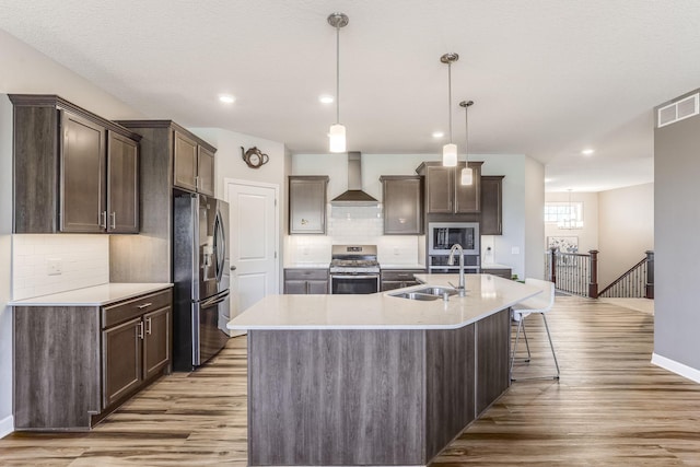 6944 Xanthus Ln N, Maple Grove, MN 55311 - kitchen featuring appliances with stainless steel finishes, wall chimney range hood, a sink, dark brown cabinetry, and light wood-type flooring