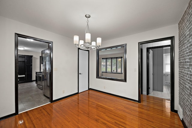 11627 Yukon St NW, Coon Rapids, MN 55433 - unfurnished dining area with a chandelier, wood finished floors, baseboards, and brick wall