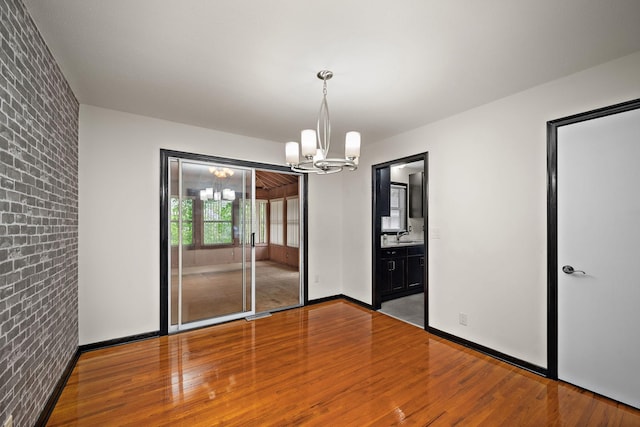 11627 Yukon St NW, Coon Rapids, MN 55433 - unfurnished dining area featuring a chandelier, wood finished floors, brick wall, and baseboards